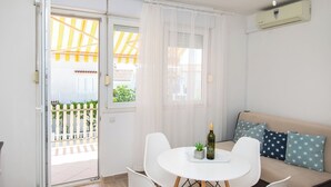A room with a white sofa, a round table with chairs, a bottle of wine, and a small plant. - Apartments Tiho (Vodice)