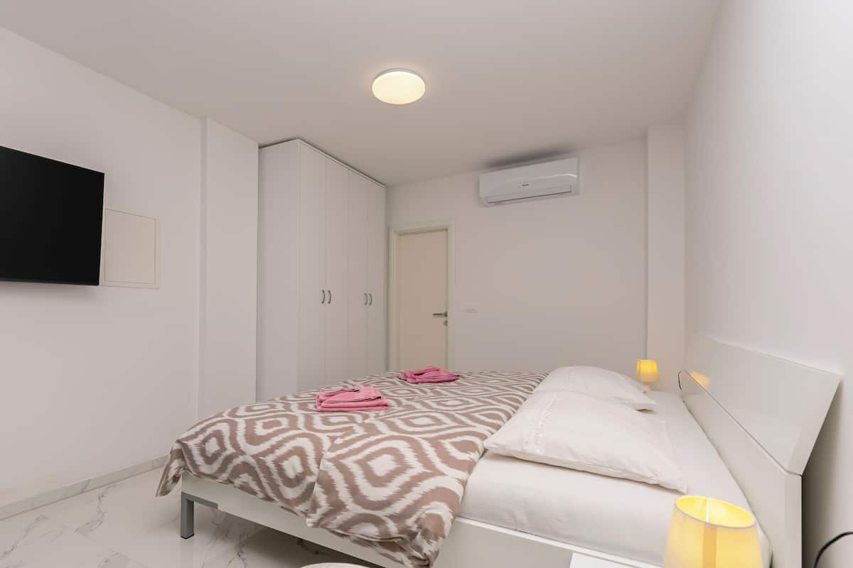 A bedroom with a bed, pillows, a bedside lamp, a flat-screen TV, and a wardrobe.