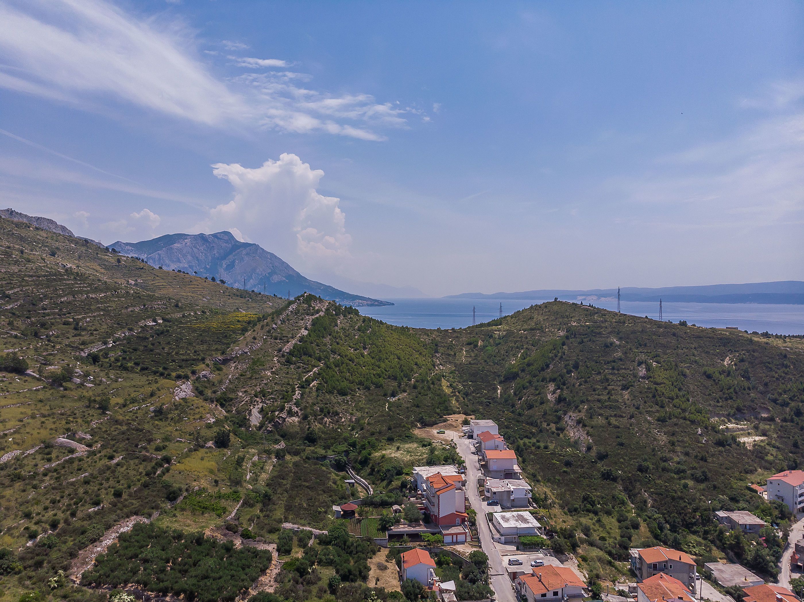 A hillside village with terraced houses, a clear view of the sea, and distant mountains.