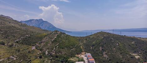 A hillside village with terraced houses, a clear view of the sea, and distant mountains.