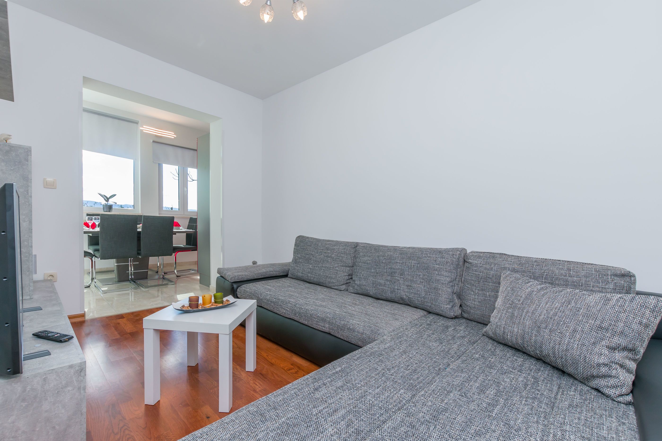 A modern living room with a grey sectional sofa, a small white table, and a remote control on the floor.