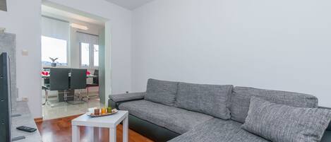 A modern living room with a grey sectional sofa, a small white table, and a remote control on the floor.