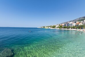 Un pueblo costero con mar azul cristalino, playa arenosa y edificios a lo largo de la costa.