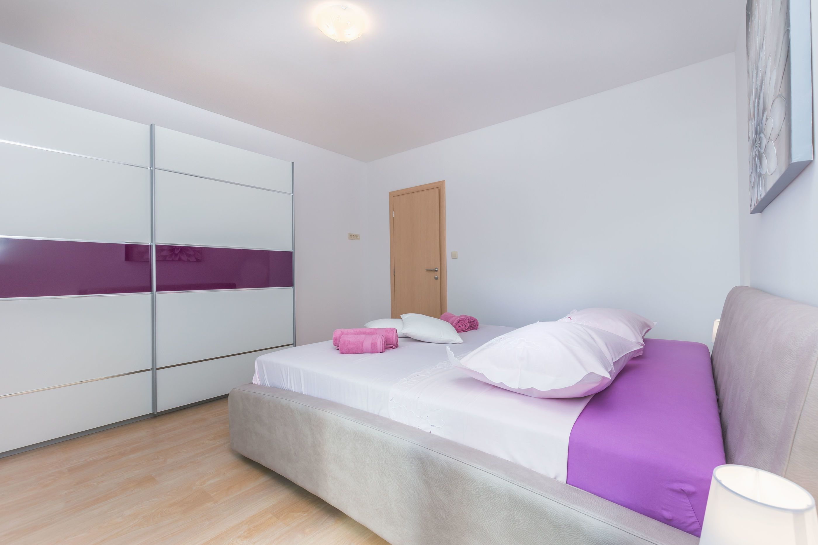 A bedroom with a bed, a wardrobe, a door, and a wall-mounted artwork.
