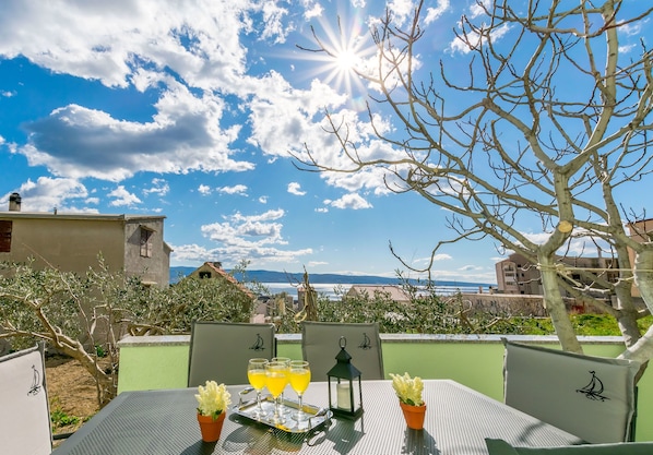 Mesa al aire libre con vista al mar, un árbol y edificios al fondo.