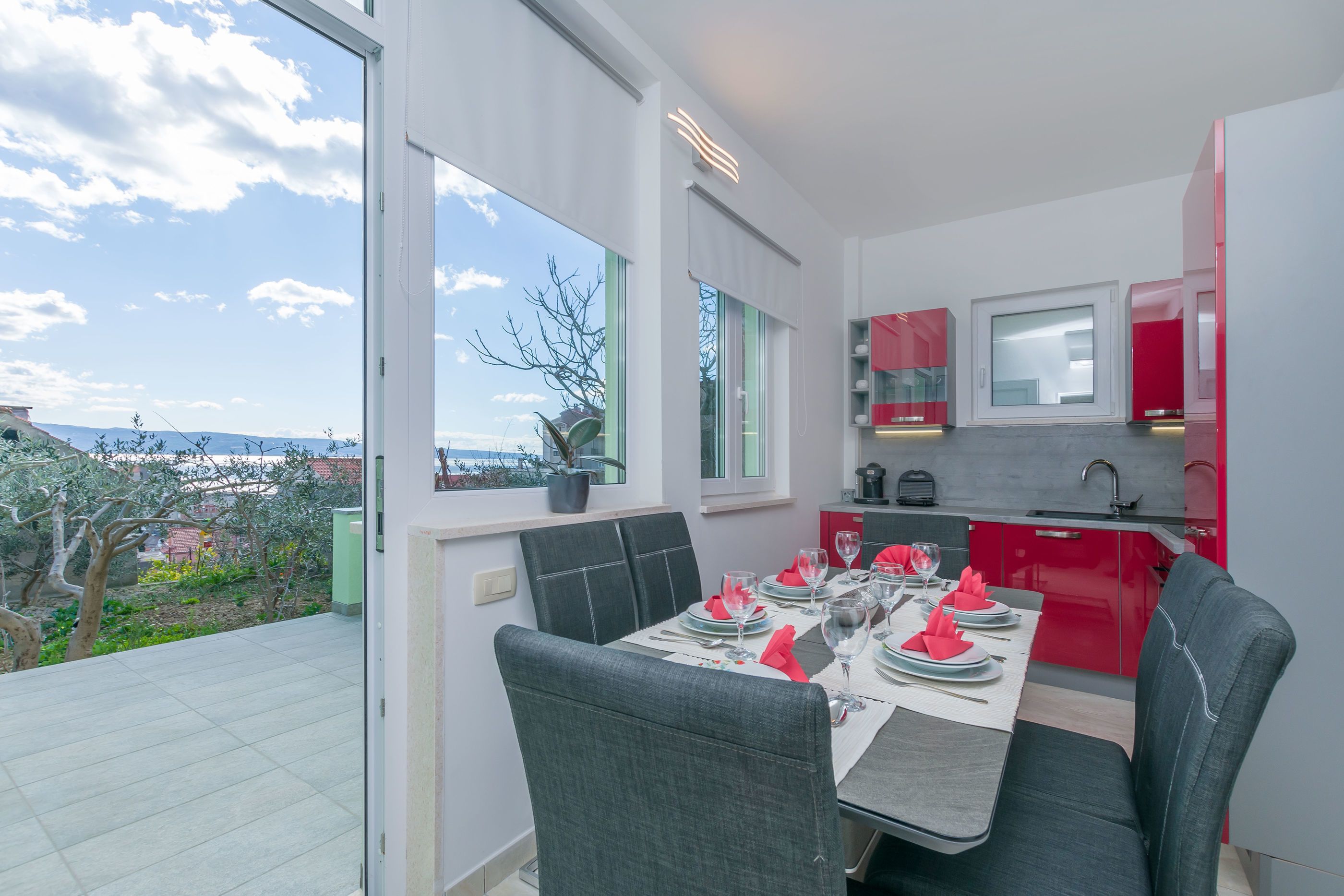 Un coin repas avec une table dressée pour quatre personnes, une cuisine aux placards rouges et une vue sur l’extérieur.