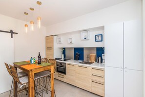 A modern kitchen with wooden cabinets, a dining table with chairs, and pendant lights.