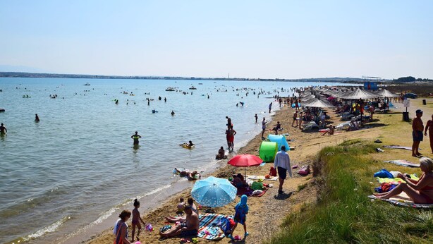 Una playa concurrida donde personas nadan y toman el sol.