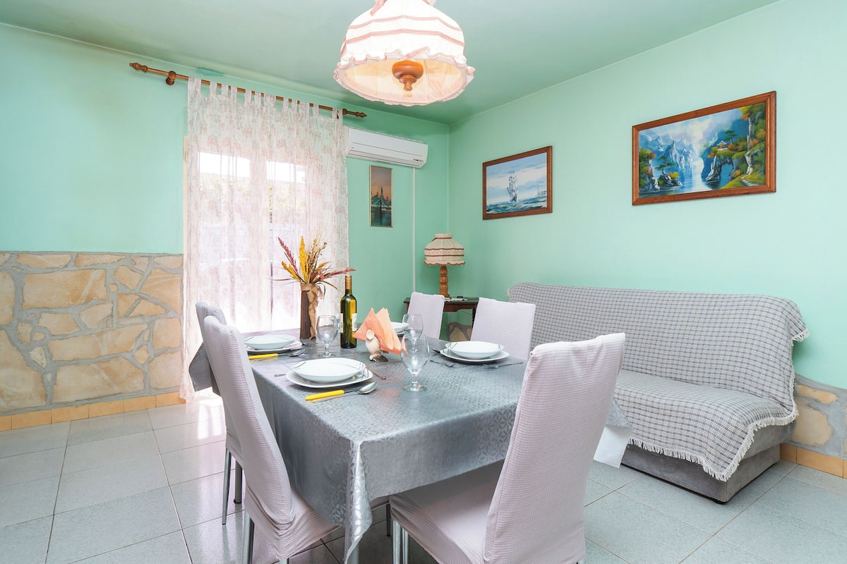 A dining area with a table set for four, a sofa, a painting, and a stone wall.