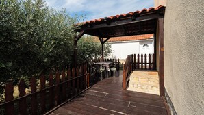 Una terraza de madera que conduce a un porche cubierto con piso de piedra y una puerta blanca.