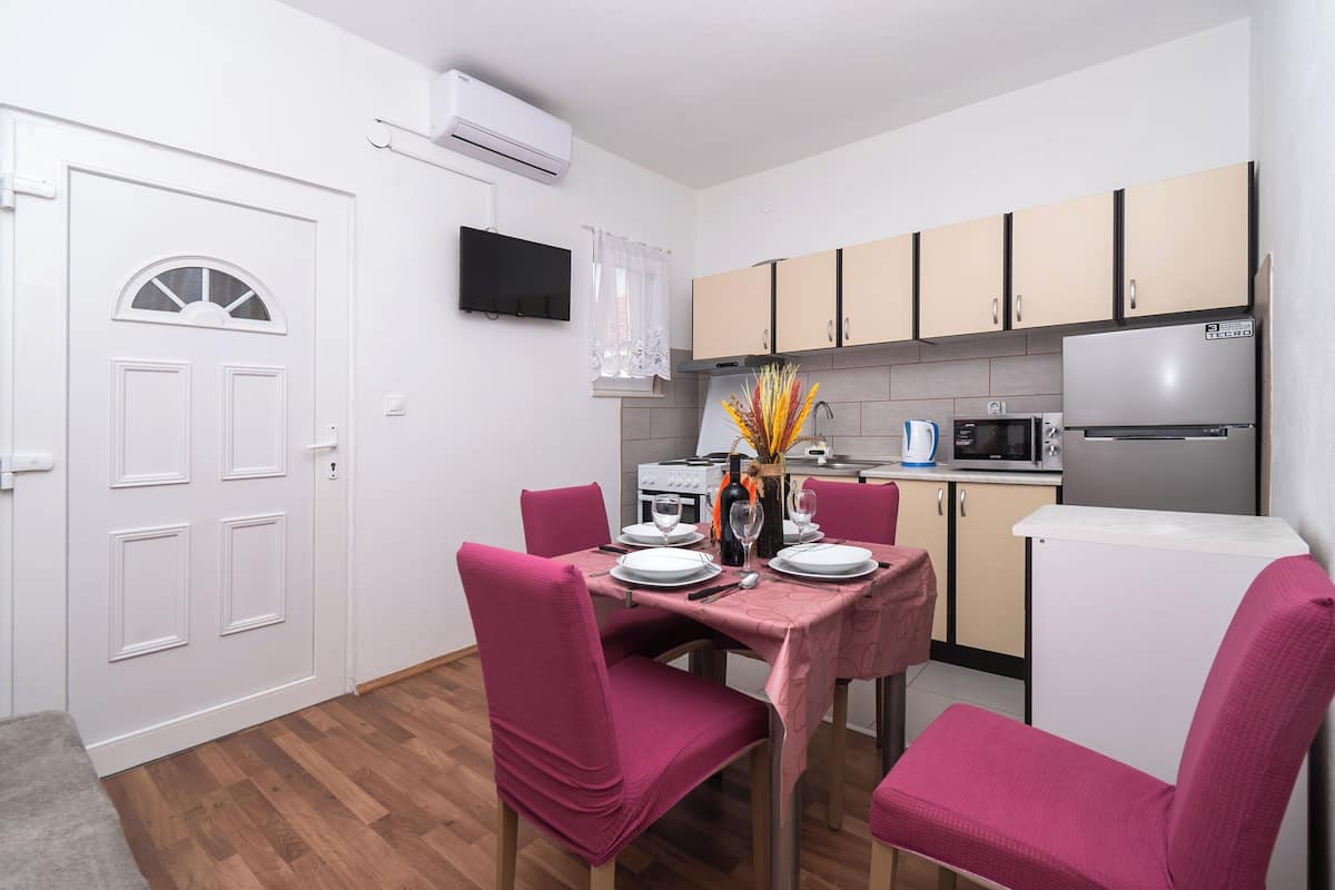 A compact kitchen with modern appliances, a dining area with pink chairs, and a white door.
