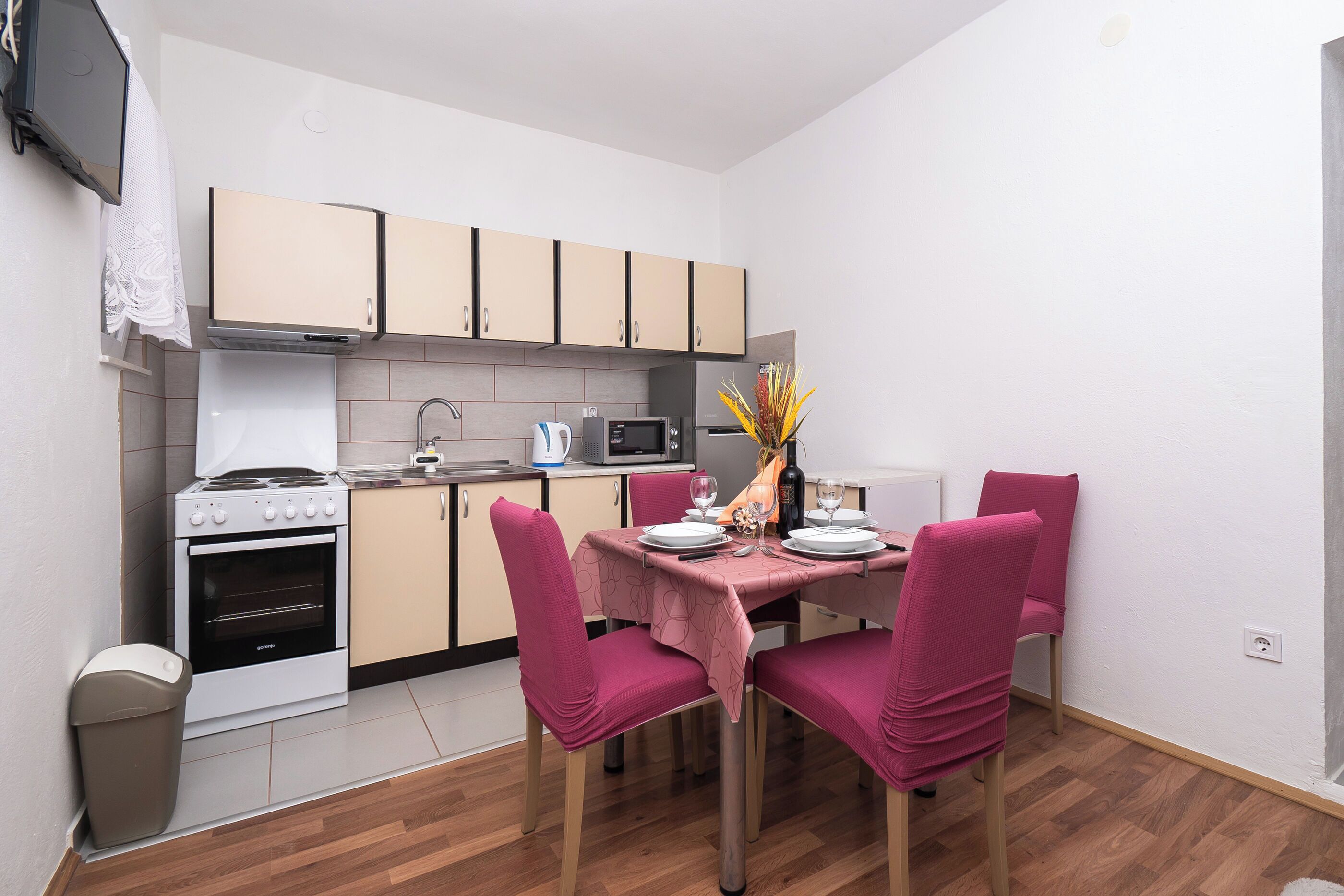 A compact kitchen with a stove, oven, microwave, and cabinets. There is a dining table with pink chairs and a vase with flowers.