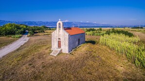 Una pequeña iglesia de piedra con techo rojo, rodeada de campos abiertos y un cielo azul despejado.