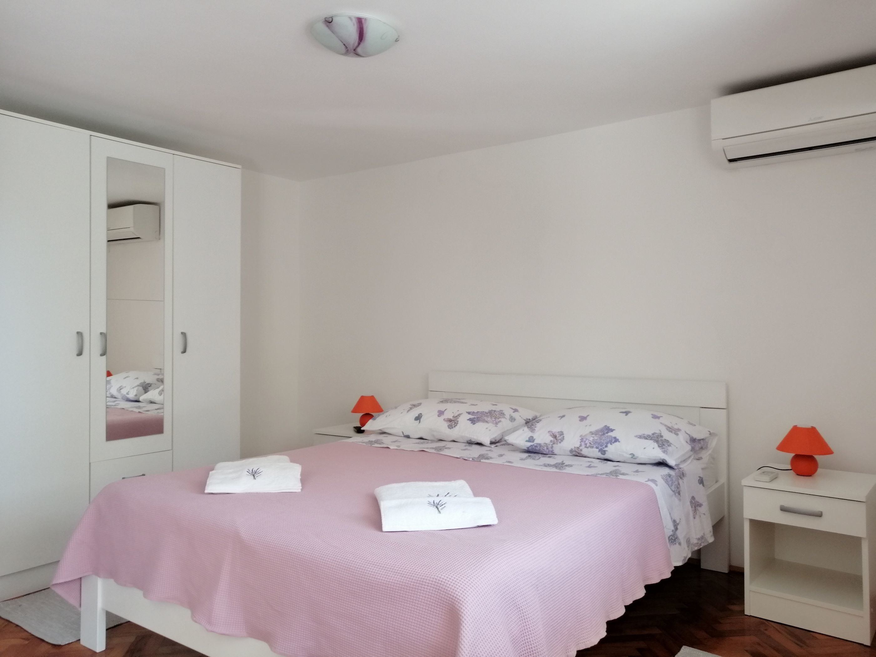 A bedroom with a bed, a wardrobe, a nightstand, and an air conditioning unit.