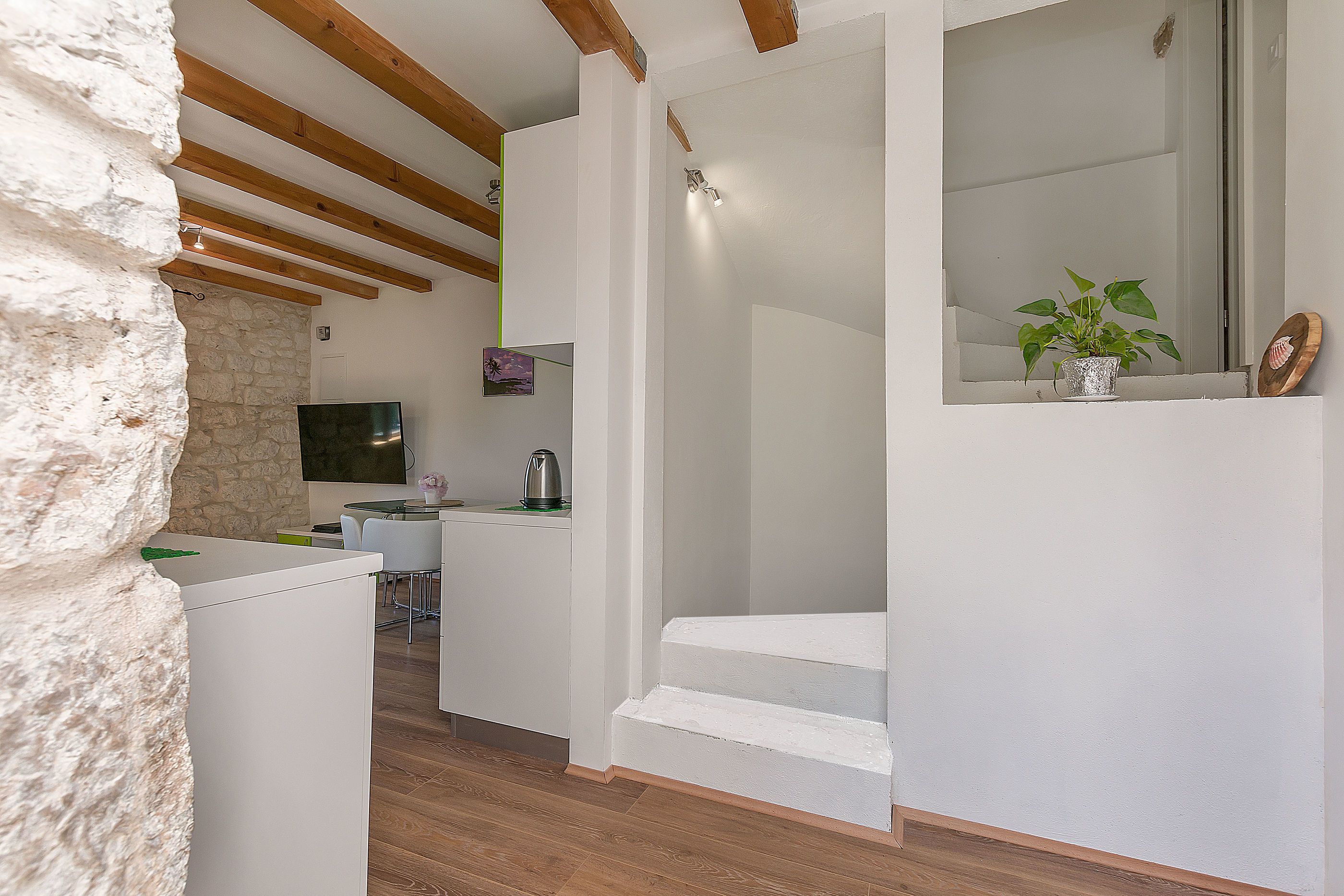 A modern interior with a stone wall, wooden beams, a staircase, a kitchen area, and a dining space.