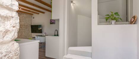 A modern interior with a stone wall, wooden beams, a staircase, a kitchen area, and a dining space.