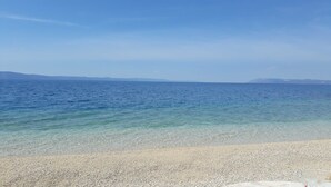 A pebbled beach with clear blue water and distant mountains. - Apartments Matko (Podgora)