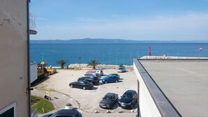 A parking lot with several cars, a view of the sea, and a distant mountain range. - Apartments Matko (Podgora)
