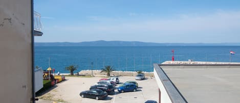A parking lot with several cars, a view of the sea, and a distant mountain range.