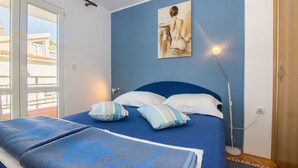 A bedroom with a bed, pillows, a painting, a bedside lamp, and a view through a door. - Apartments Matko (Podgora)