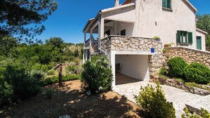 Una casa de dos pisos con fachada de piedra, un balcón y un jardín con diversas plantas y arbustos.