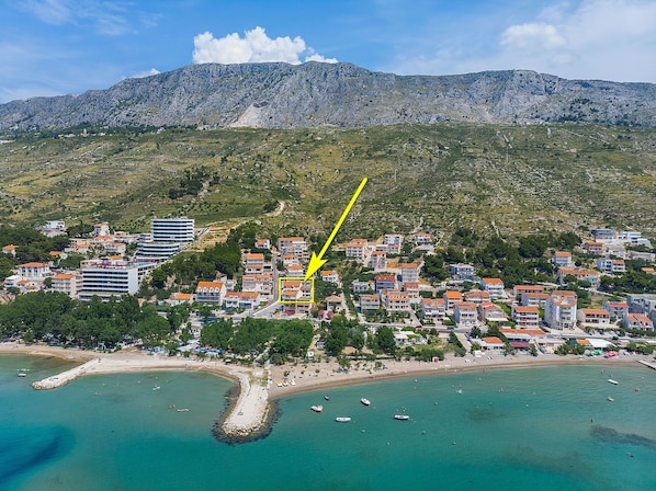 Luftaufnahme einer Küstenstadt mit Gebäuden, einem Strand und einem Bergpanorama im Hintergrund.