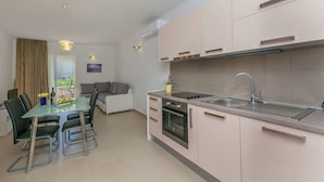 A modern kitchen with a glass dining table, black chairs, a built-in oven, and a stainless steel sink. - Apartments Villa Aquamarine (Duce)