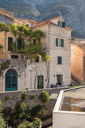 A stone building with a tiled roof, a green door, and a small balcony with a metal railing.