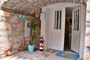 A stone wall entrance with a door, a potted plant, a small bucket, a red and white lighthouse, and a blue mat. - House Stone House Mia Casa (Stari Grad)