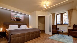 A modern hotel room with a large bed, a small table, a chair, and a window with curtains. - Apartments Menuet (Karlovy Vary)