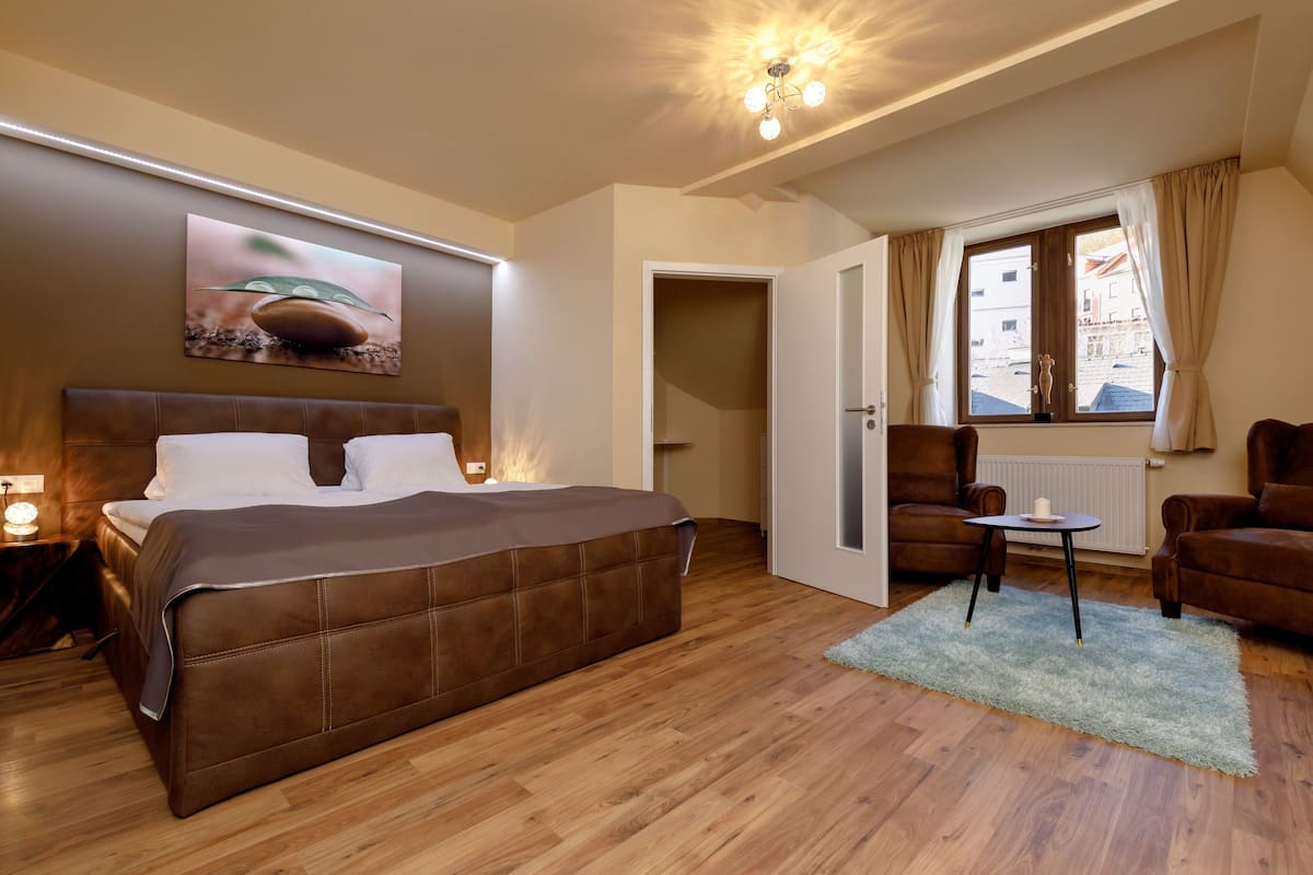 A modern hotel room with a large bed, a small table, a chair, and a window with curtains.