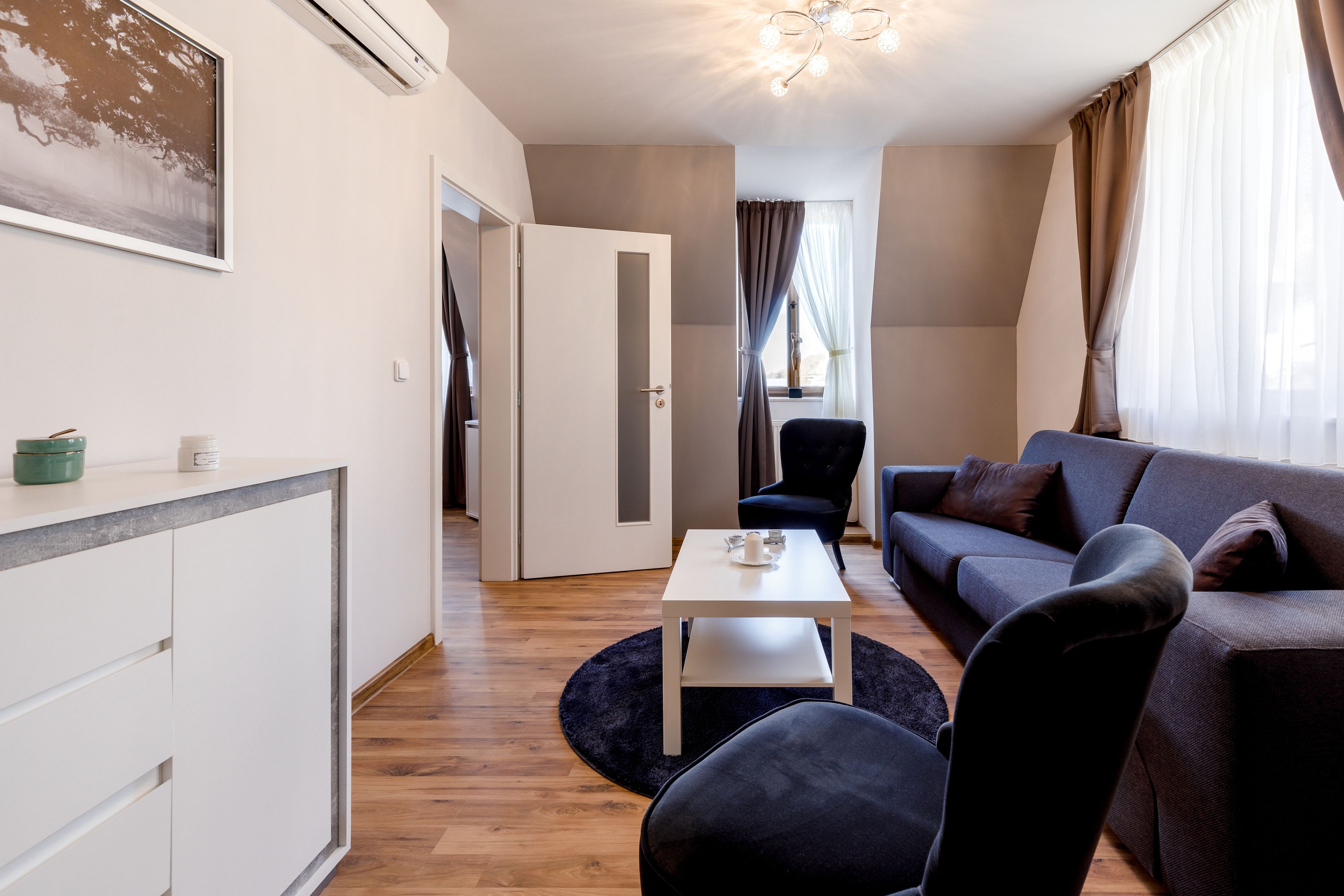 A modern living room with a sofa, a coffee table, and a chair. There is a door leading to another room.