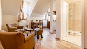 A modern living room with a dining area, a glass shower, and a view of the kitchen. - Apartments Menuet (Karlovy Vary)