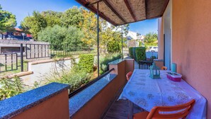Un balcón con mesa y sillas, con vistas a un jardín y edificios.