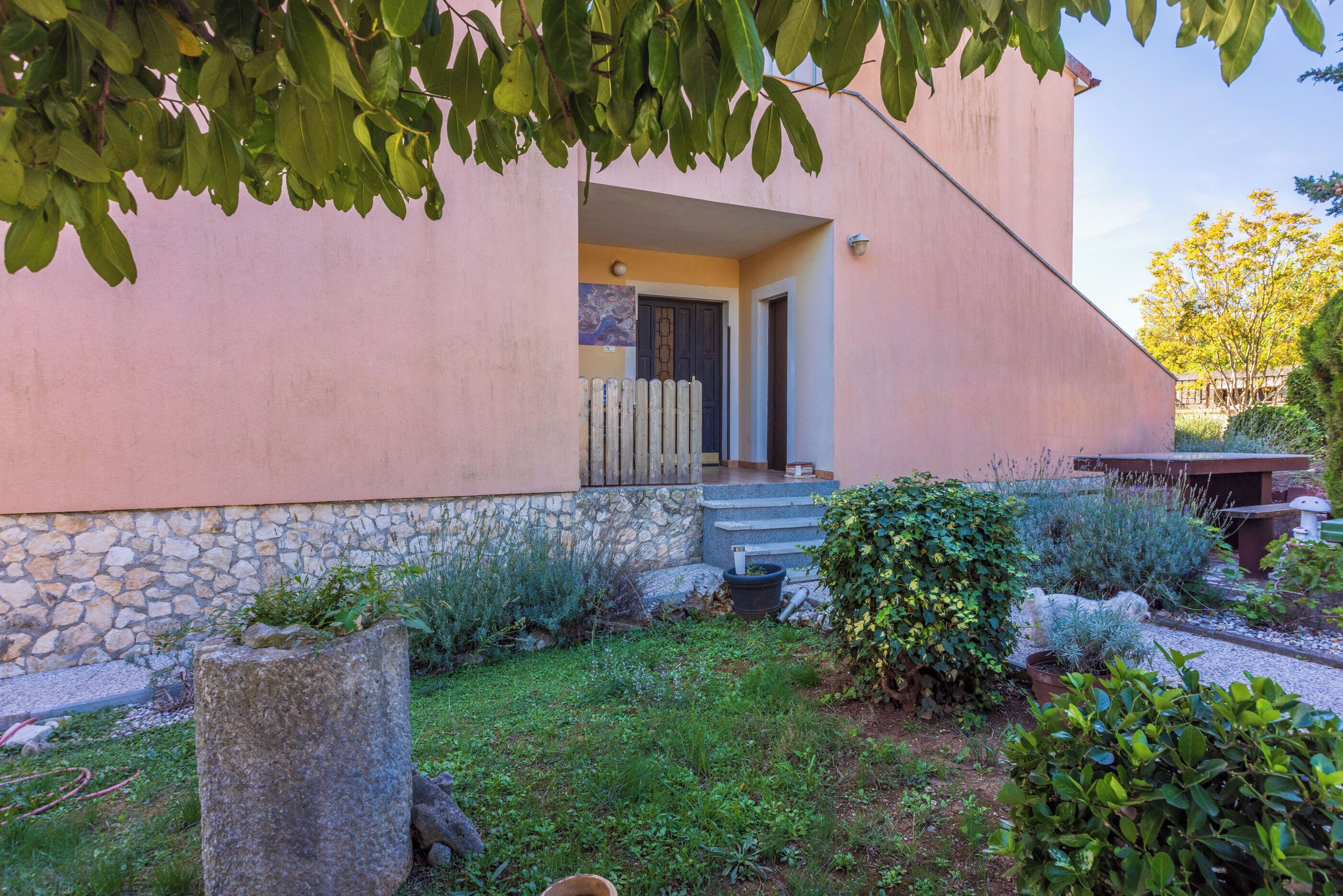 A house with a stone foundation, a pink exterior, and a small porch with steps leading to a door.