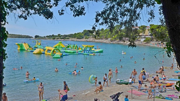 Una playa con estructuras acuáticas inflables y gente nadando y tomando el sol.