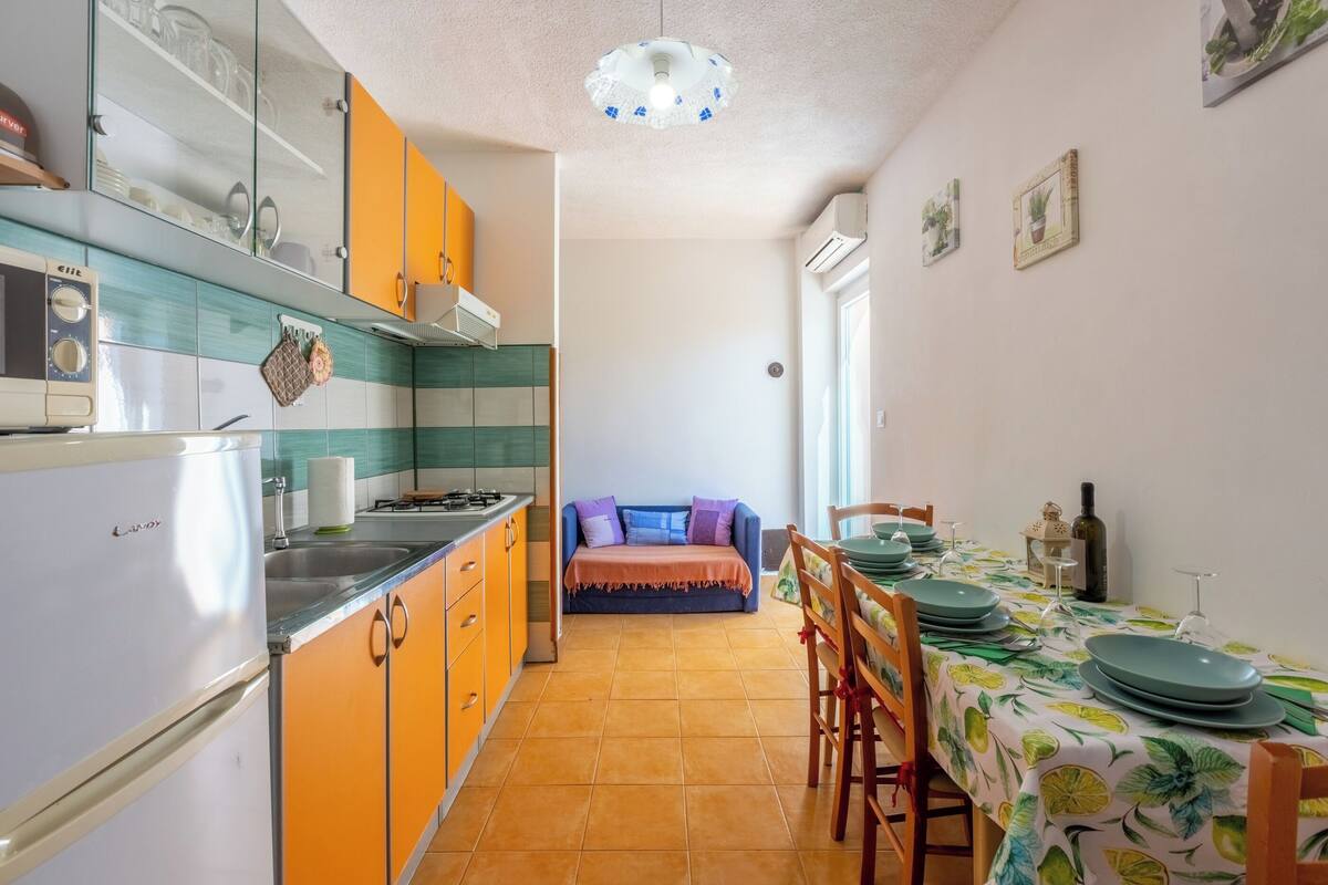 A kitchen with orange cabinets, a refrigerator, and a dining area with a table set for two.