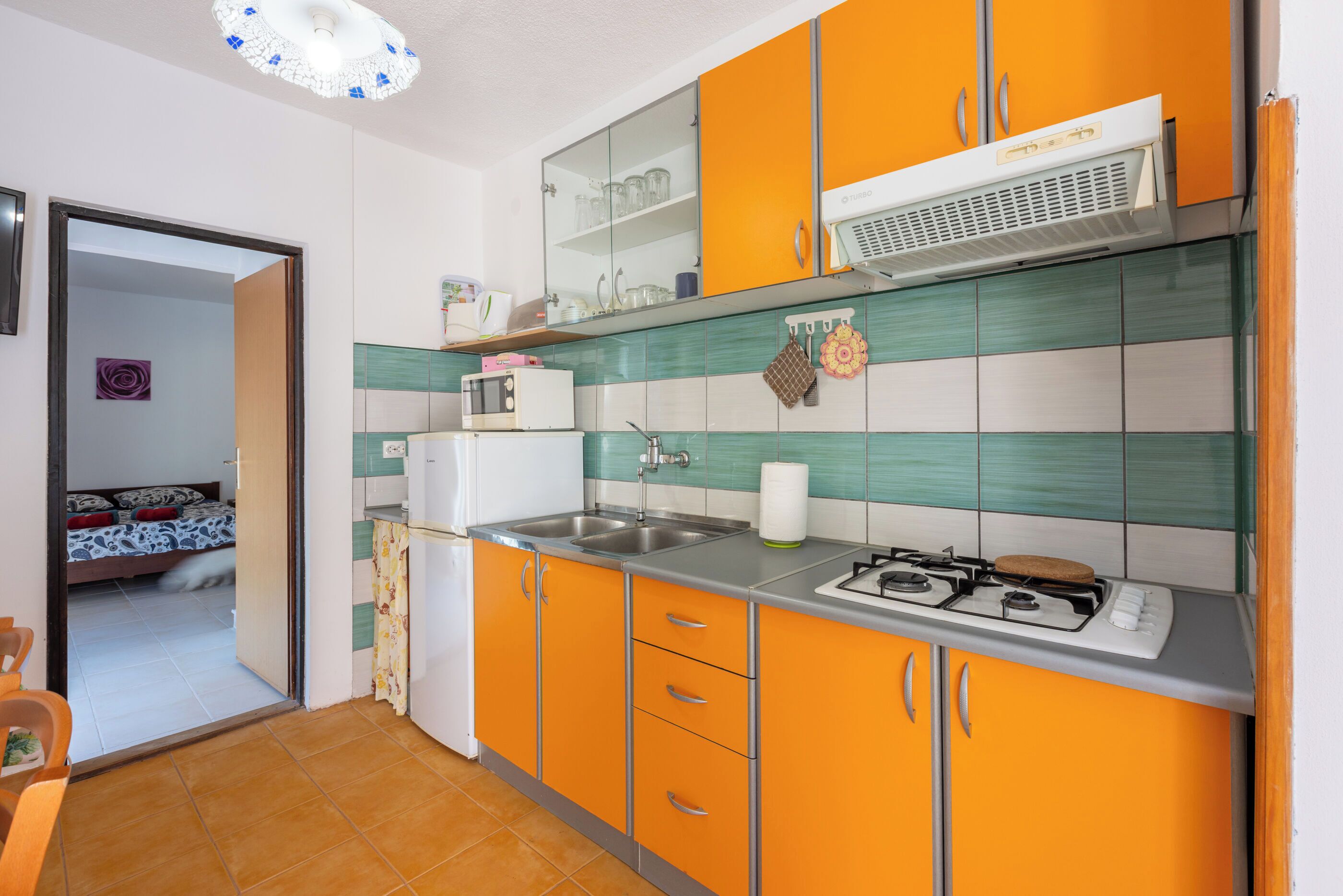 Une cuisine de taille réduite avec des meubles de couleur orange, une cuisinière à gaz et un four à micro-ondes.