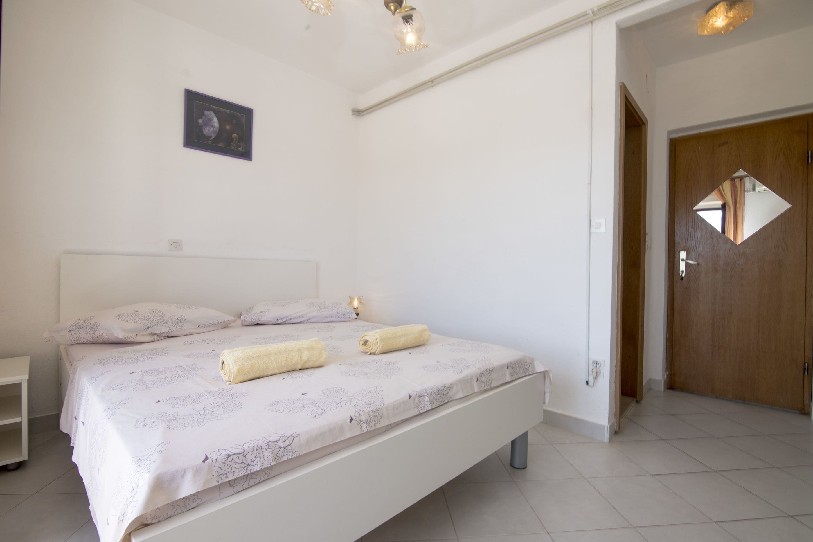 A bedroom with a bed, a nightstand, a wooden door, and a small framed picture on the wall.