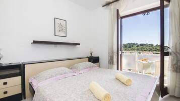 Un dormitorio con una cama grande, una mesita de noche, una lámpara de noche, un cuadro en la pared y vistas al exterior a través de un ventanal amplio.