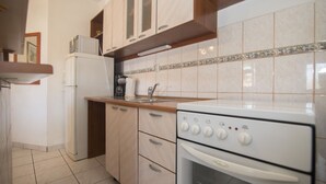 A kitchen with wooden cabinets, a white refrigerator, a stove, and a tiled backsplash. - Apartments and Rooms Nikol (Hvar)