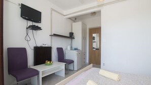 A bedroom with a bed, a desk, two chairs, a television, and a kitchenette. - Apartments and Rooms Nikol (Hvar)