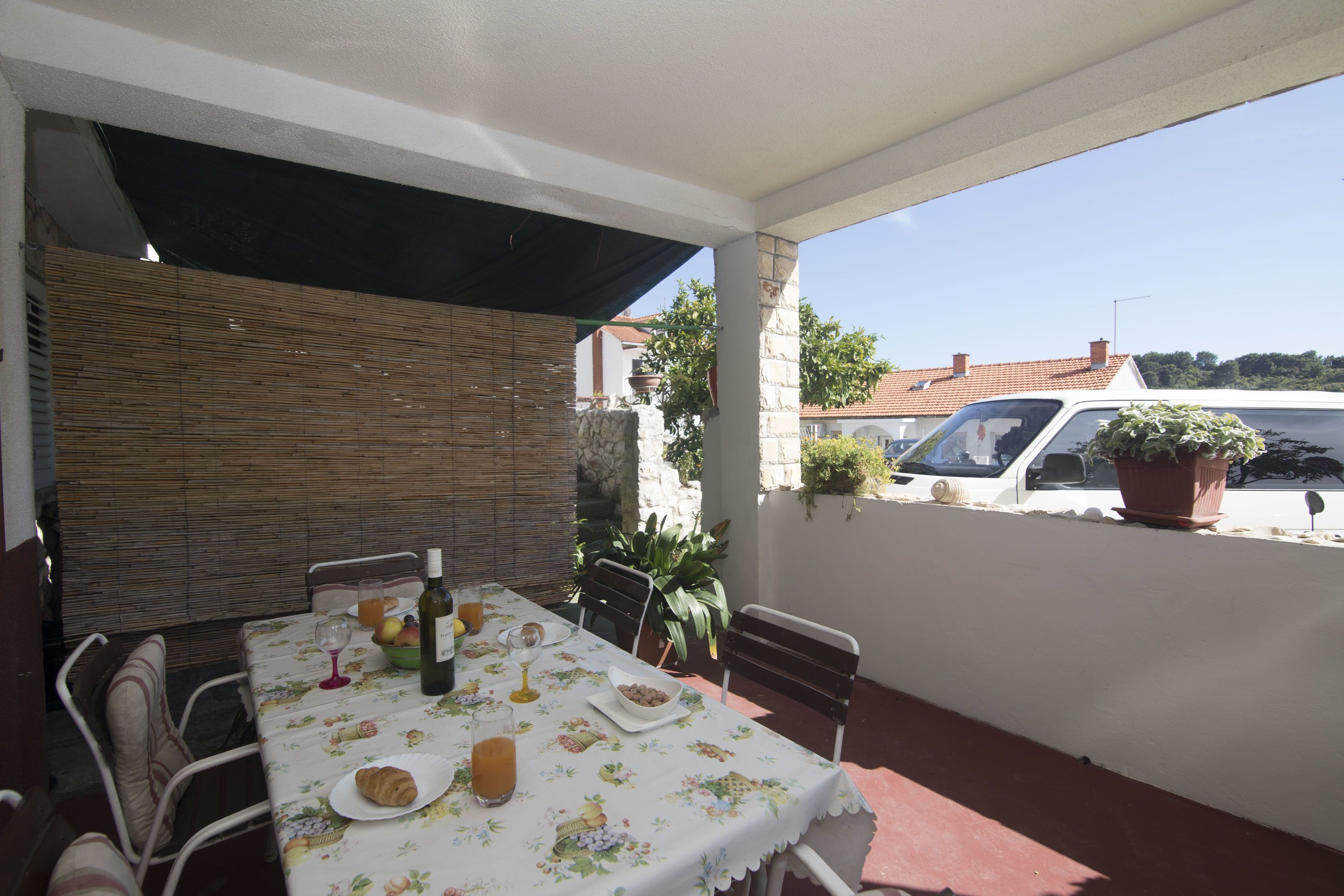 An outdoor patio with a table set for breakfast, including croissants, fruit, and beverages.