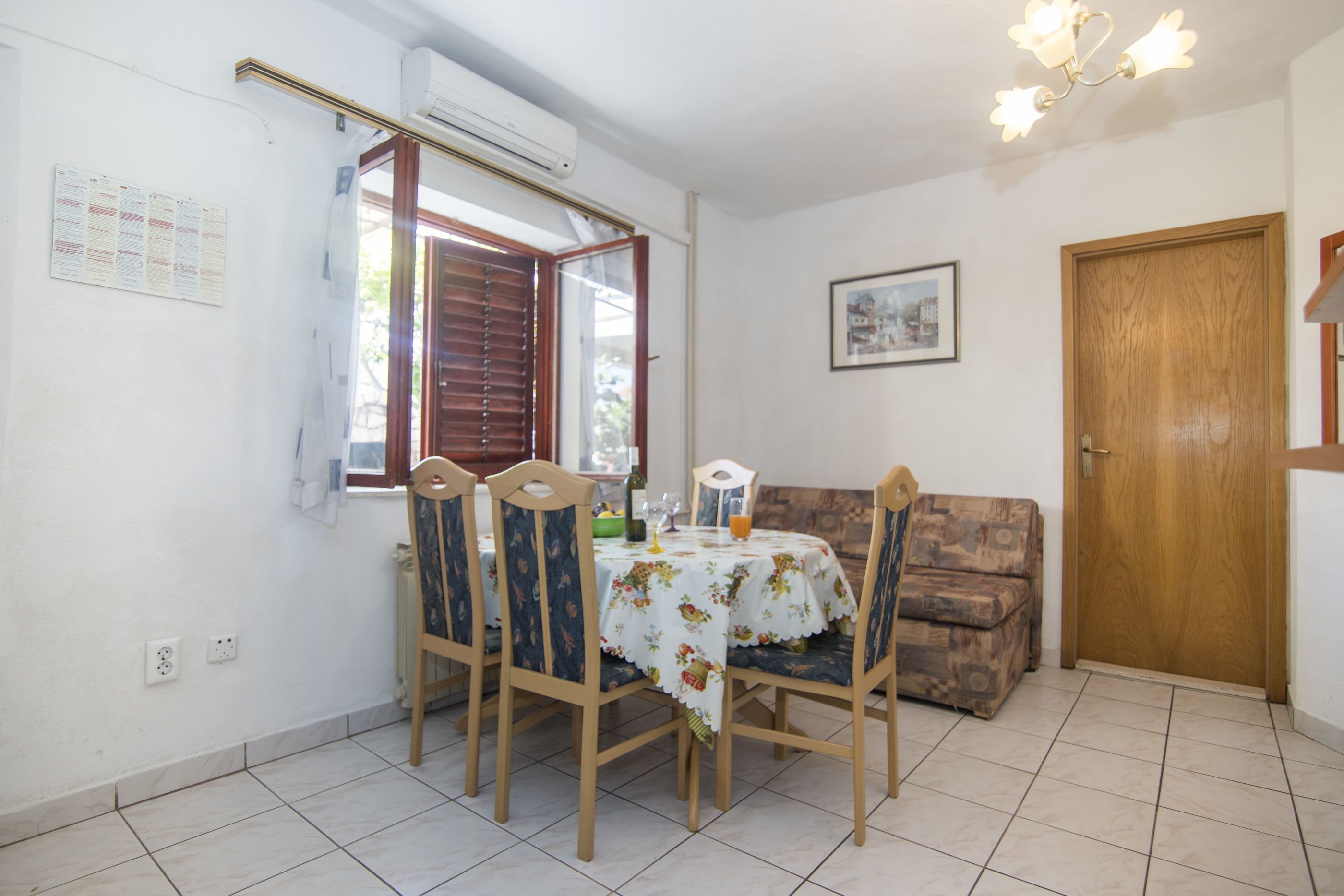 Zona de menjador amb una taula ben posada per a quatre, cadires, una porta de fusta i un aire condicionat fixat a la paret.