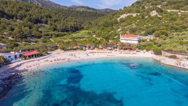 A coastal area with a beach, clear blue waters, and a building with a red roof. - Apartments and Rooms Nikol (Hvar)