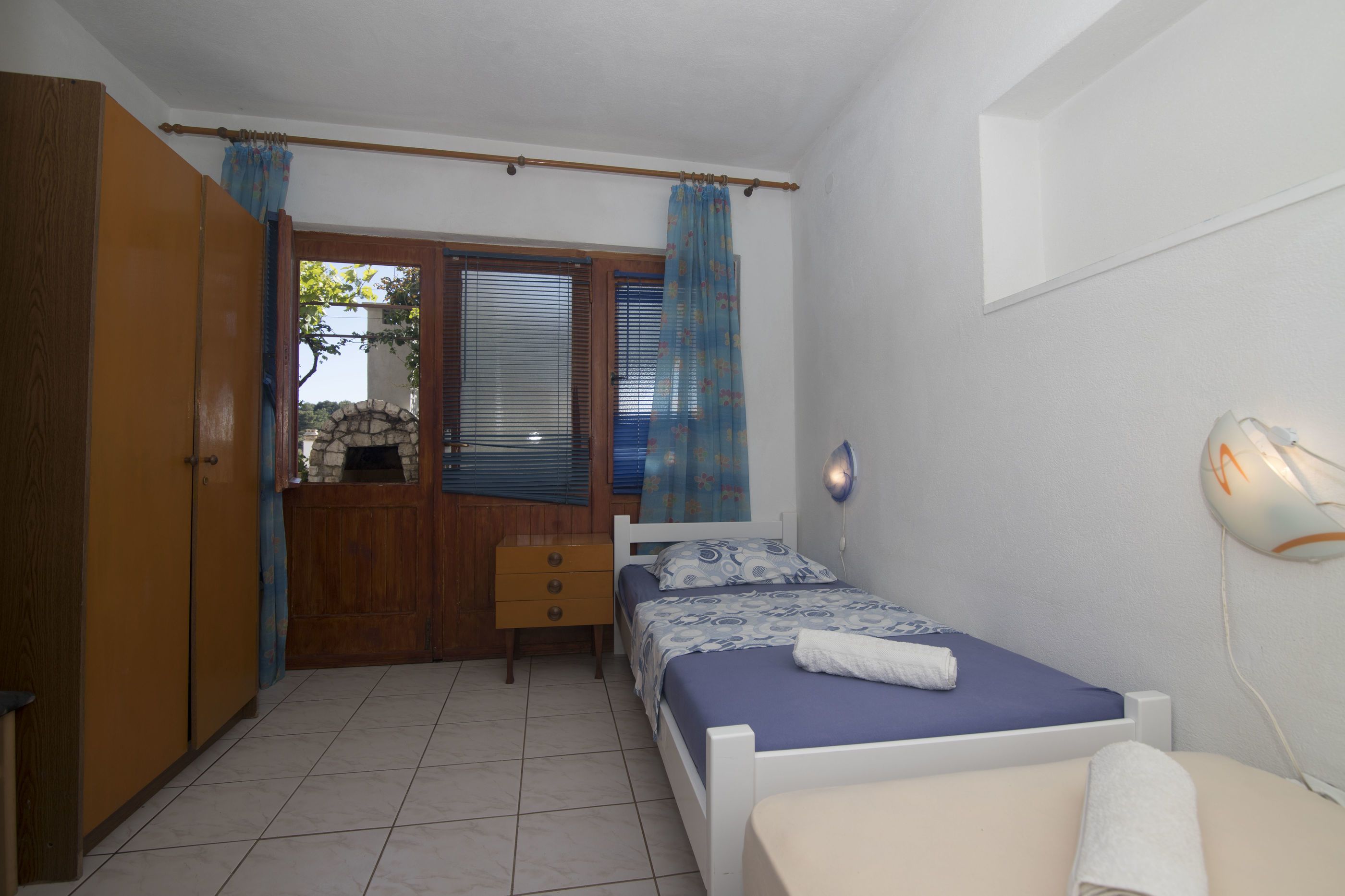 A bedroom with a bed, a wardrobe, a small table, and a window with curtains.