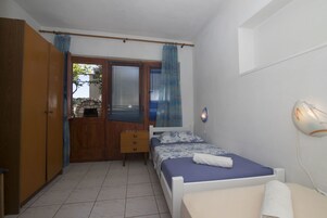 Un dormitorio con cama, armario, mesita y ventana con cortinas.
