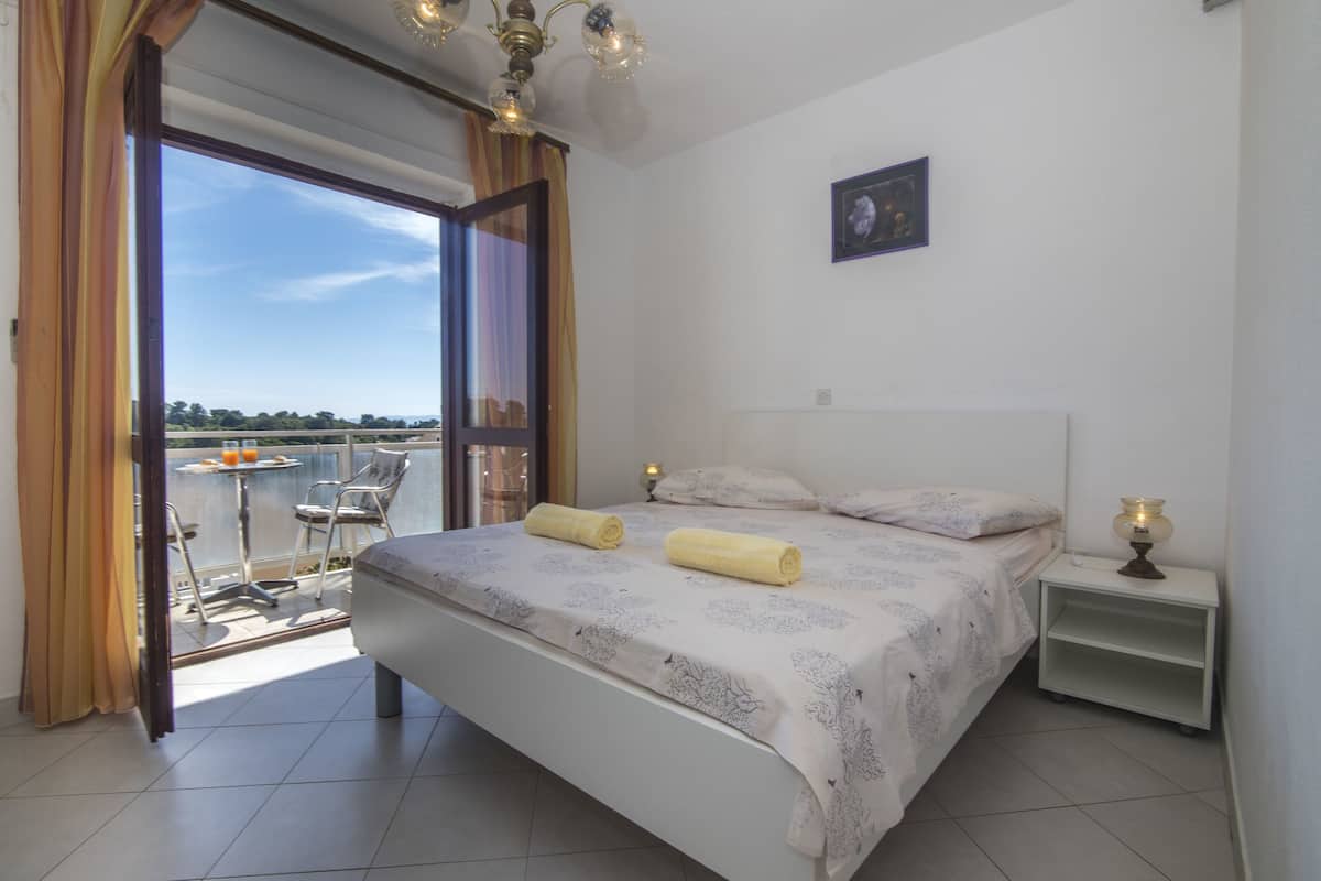 Une chambre à coucher avec un lit, une table de chevet, une fenêtre avec des rideaux et une vue sur l’extérieur.