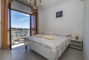 Un dormitorio con cama, mesita de noche, ventana con cortinas y vistas al exterior.