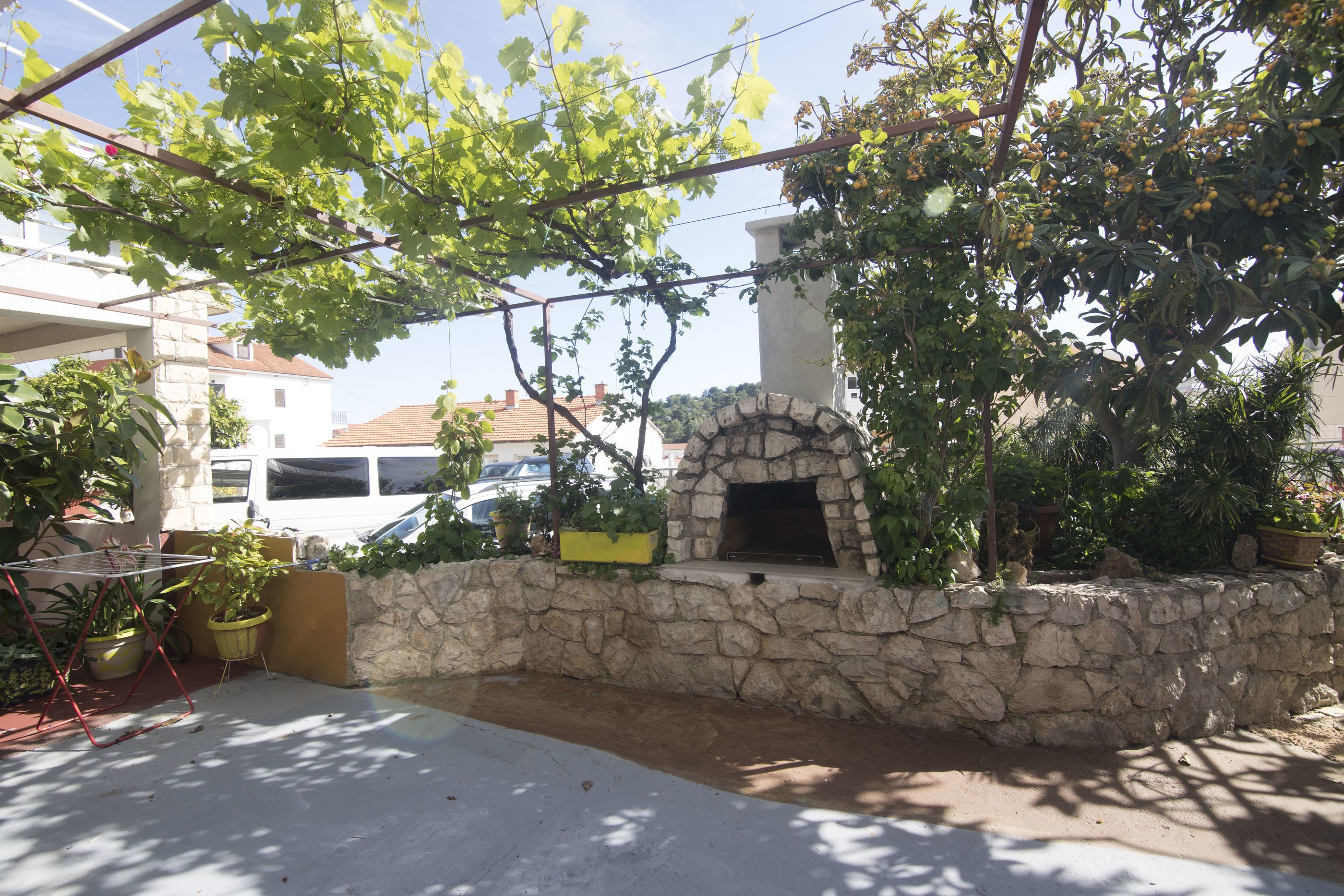 Una pared de piedra con chimenea integrada, plantas en macetas y una estructura colgante para plantas.
